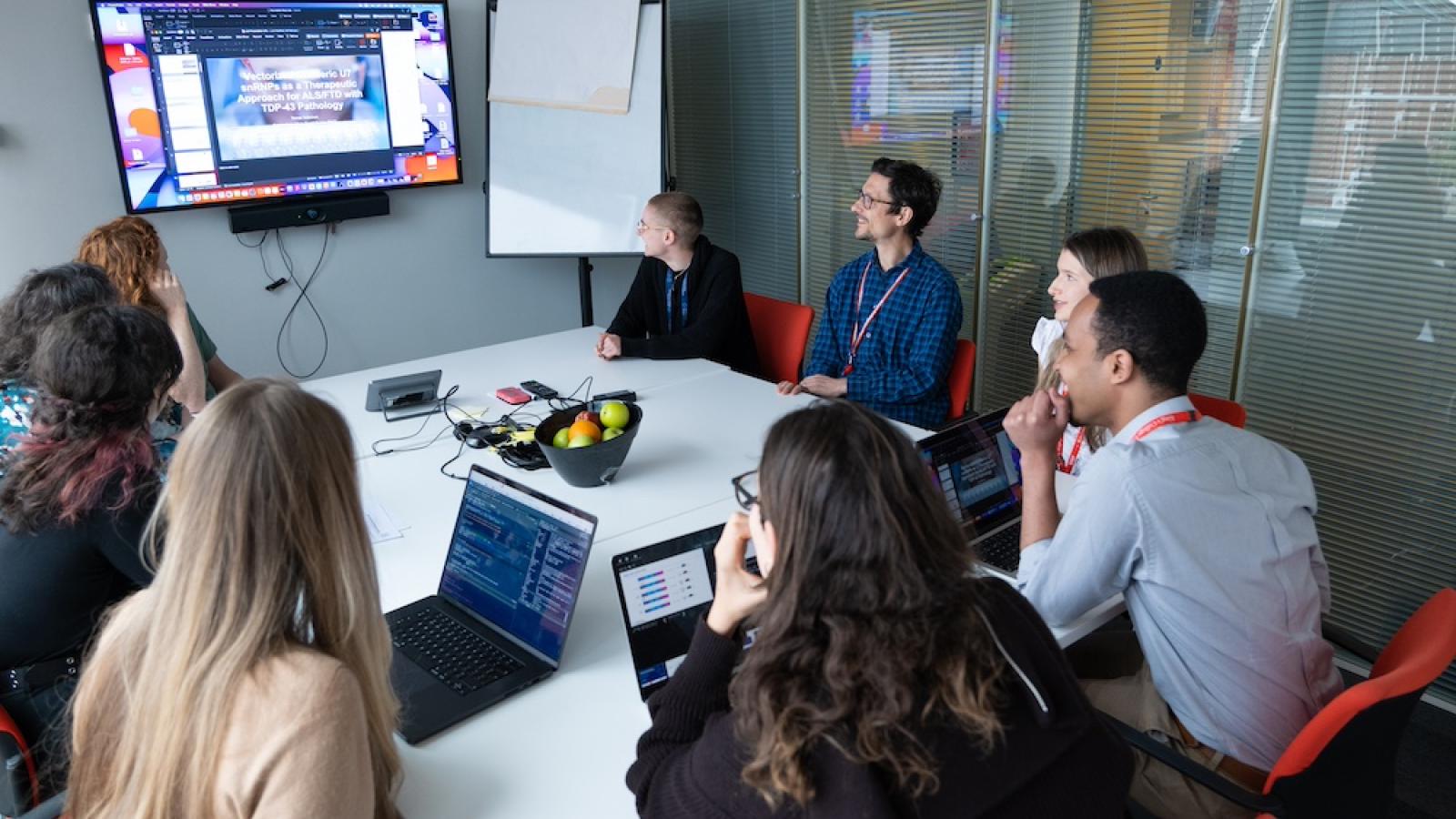 Researchers sit around a table looking at a powerpoint presentation