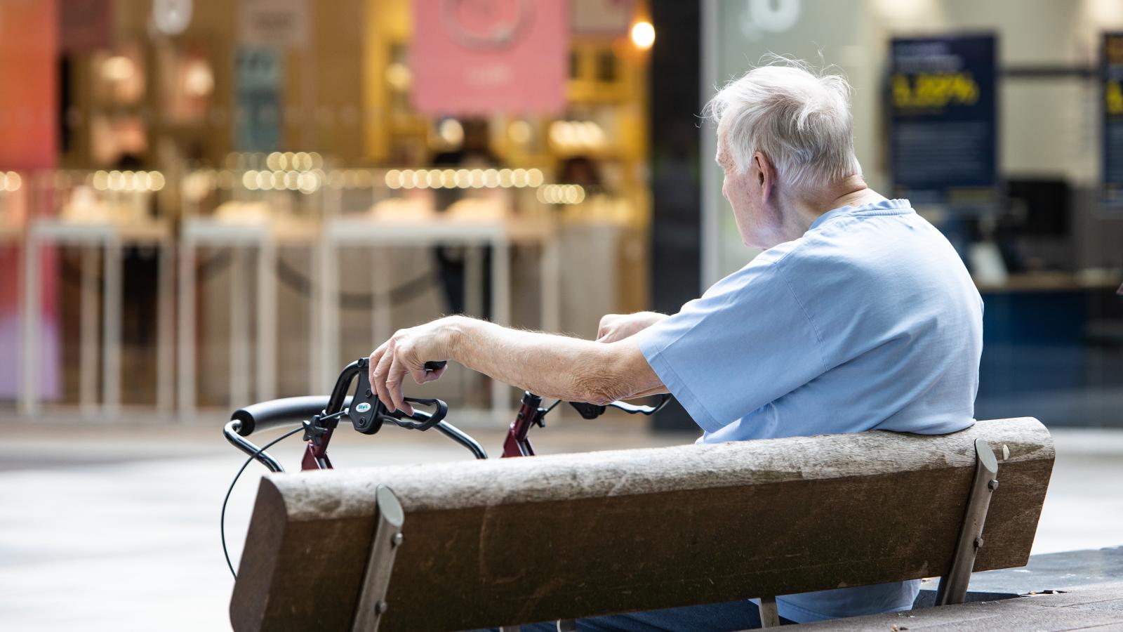 A man with a walking aid sits on a public bench