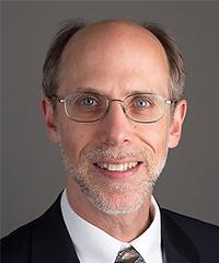 Man with grey/brown hair, stubble and glasses