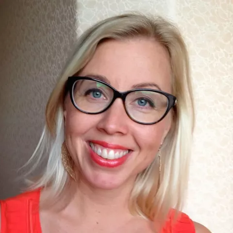 Female with shoulder length blonde hair and black framed glasses