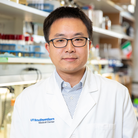 Male with short black hair and glasses wearing a lab coat, in a lab