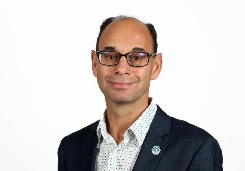 Male with glasses wearing a white shirt with black dots and a black suit jacket