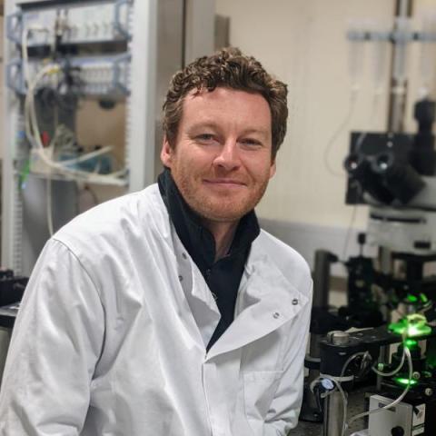 Male with curly brown hair, wearing a lab coat