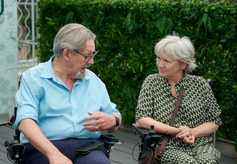 Two people sit in wheelchairs next to one another