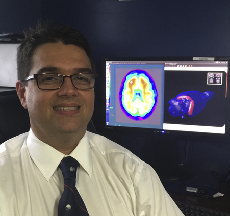 A picture of Pedro Rosa-Neto with colourful brain scan on screen in background