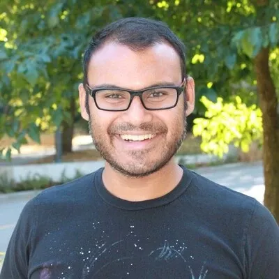 Smiling male with dark hair, facial hair and glasses