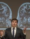 Male with dark hair, lecturing in front some brain scans