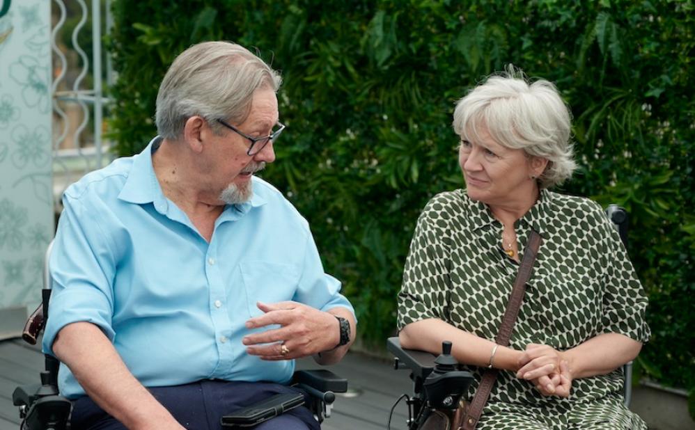 Two people sit in wheelchairs next to one another