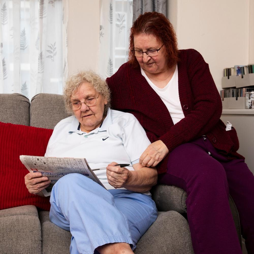 Two women doing a crossword on a sofa