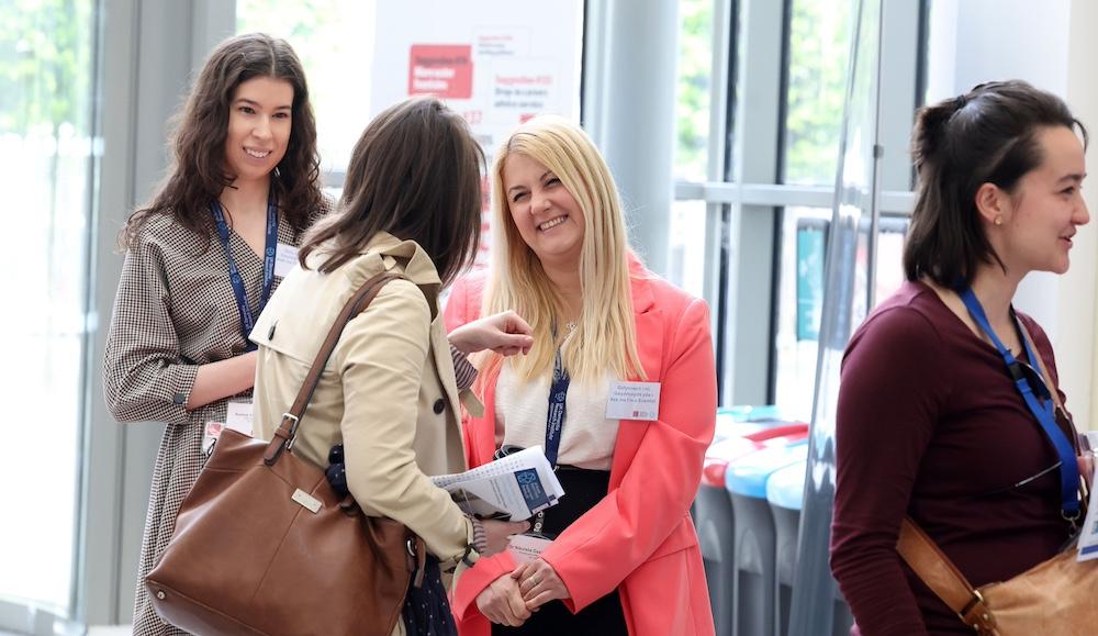 Four women at a conference networking and smiling in a bright, indoor space.