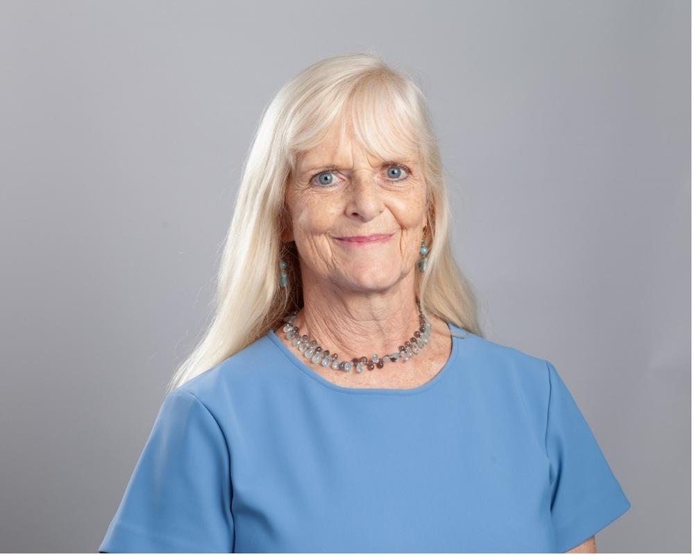 Female with long white-blonde hair and a fringe with a blue top and necklace