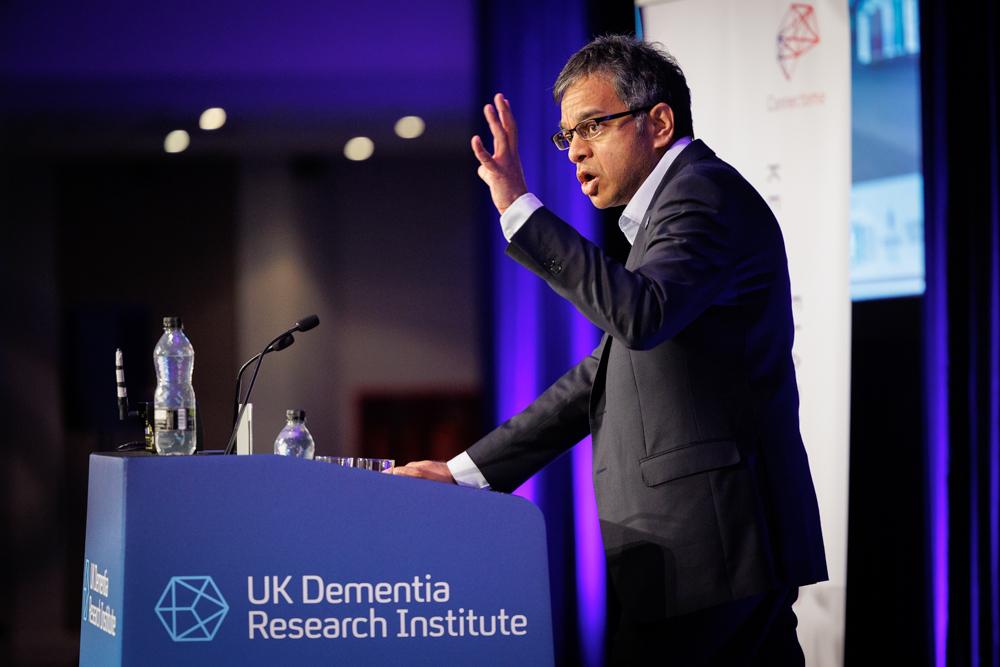 Prof Siddharthan chandran stands on a stage at a conference.