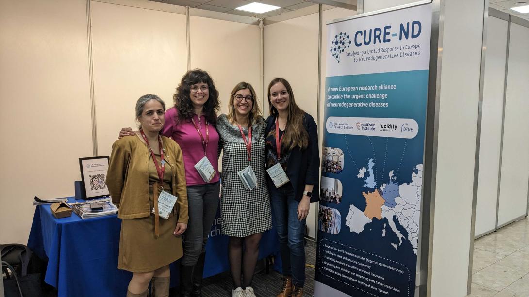 Four people stand in front of a stand at a scientific conference